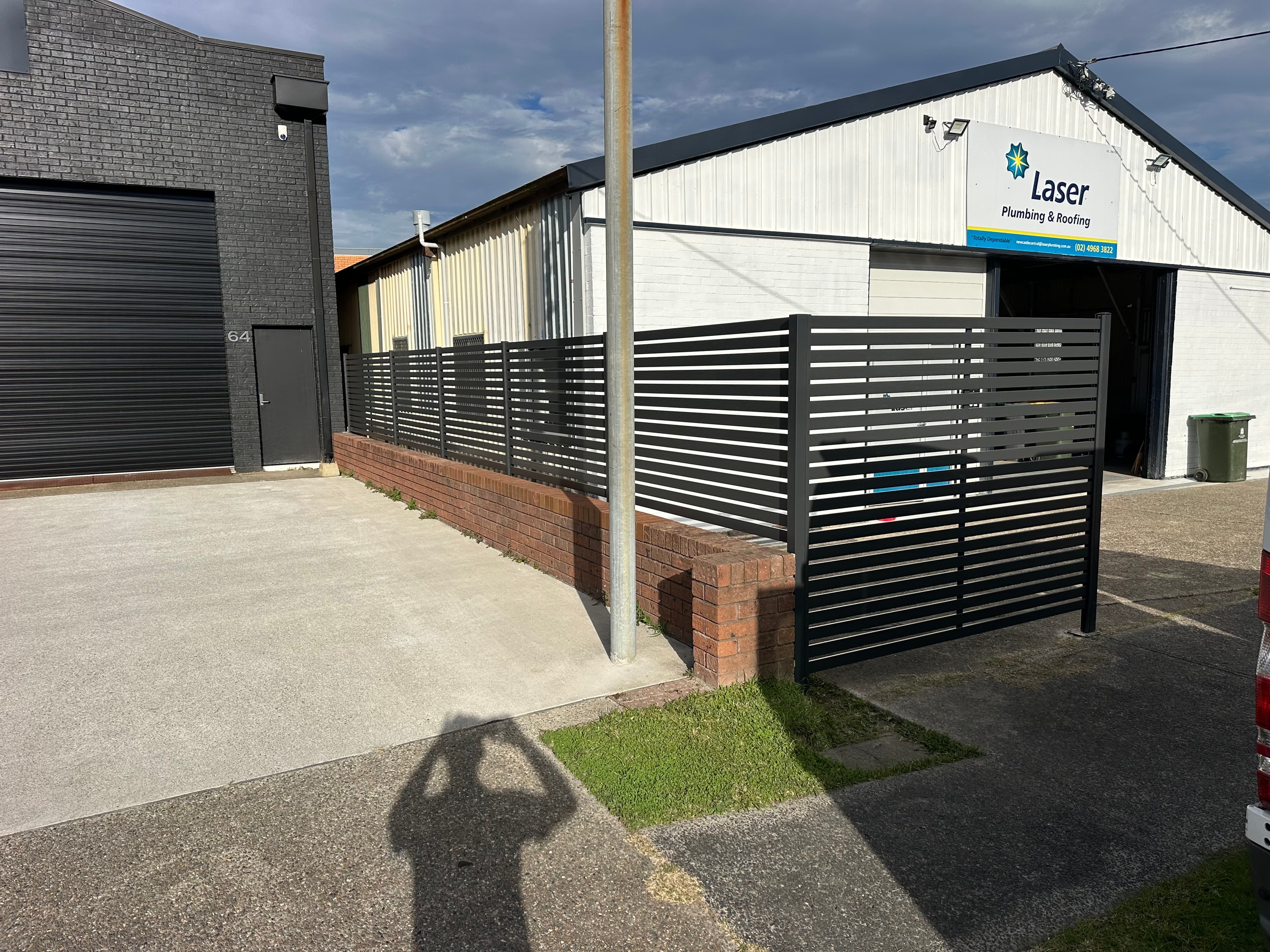 Charcoal aluminium horizontal slat fence on brick base — commercial driveway