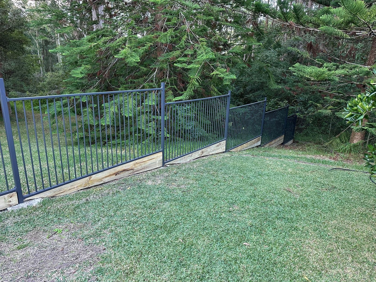 Black tubular steel fence on treated pine sleeper retaining base — sloped block